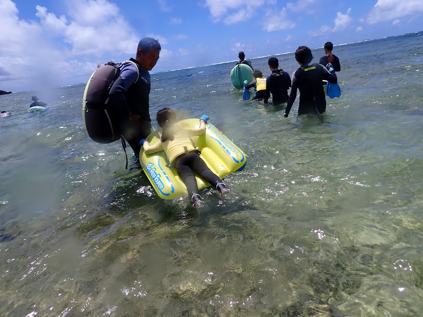 浅瀬でフロートに寄りかかりスタッフに付き添われ海に入る参加者