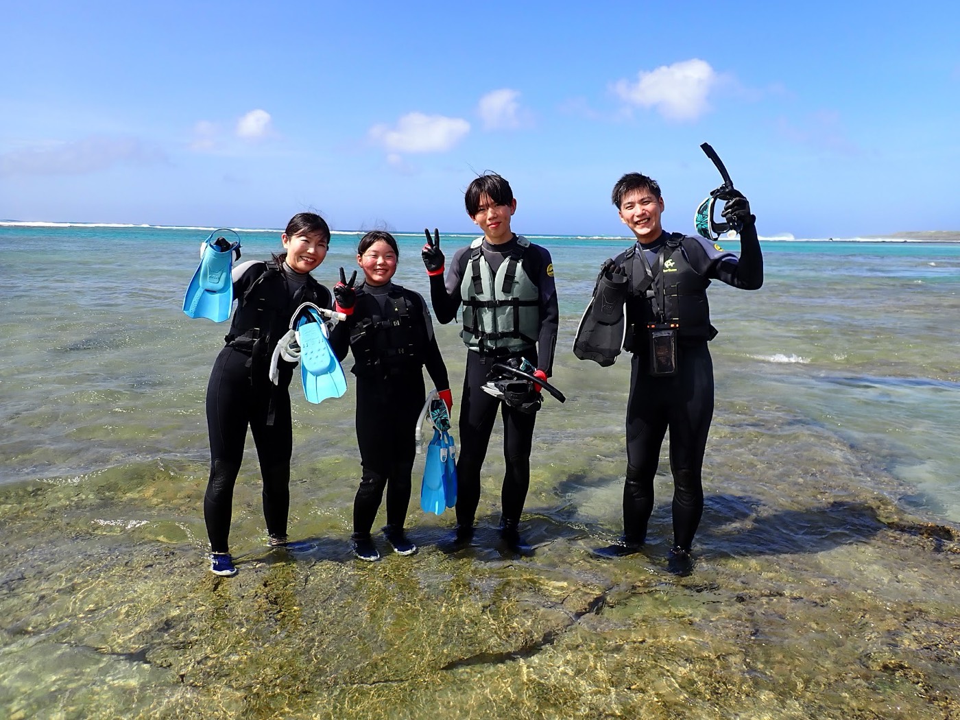 浜辺でウェットスーツを着てマスクとフィンを手に笑顔でポーズをとる参加者
