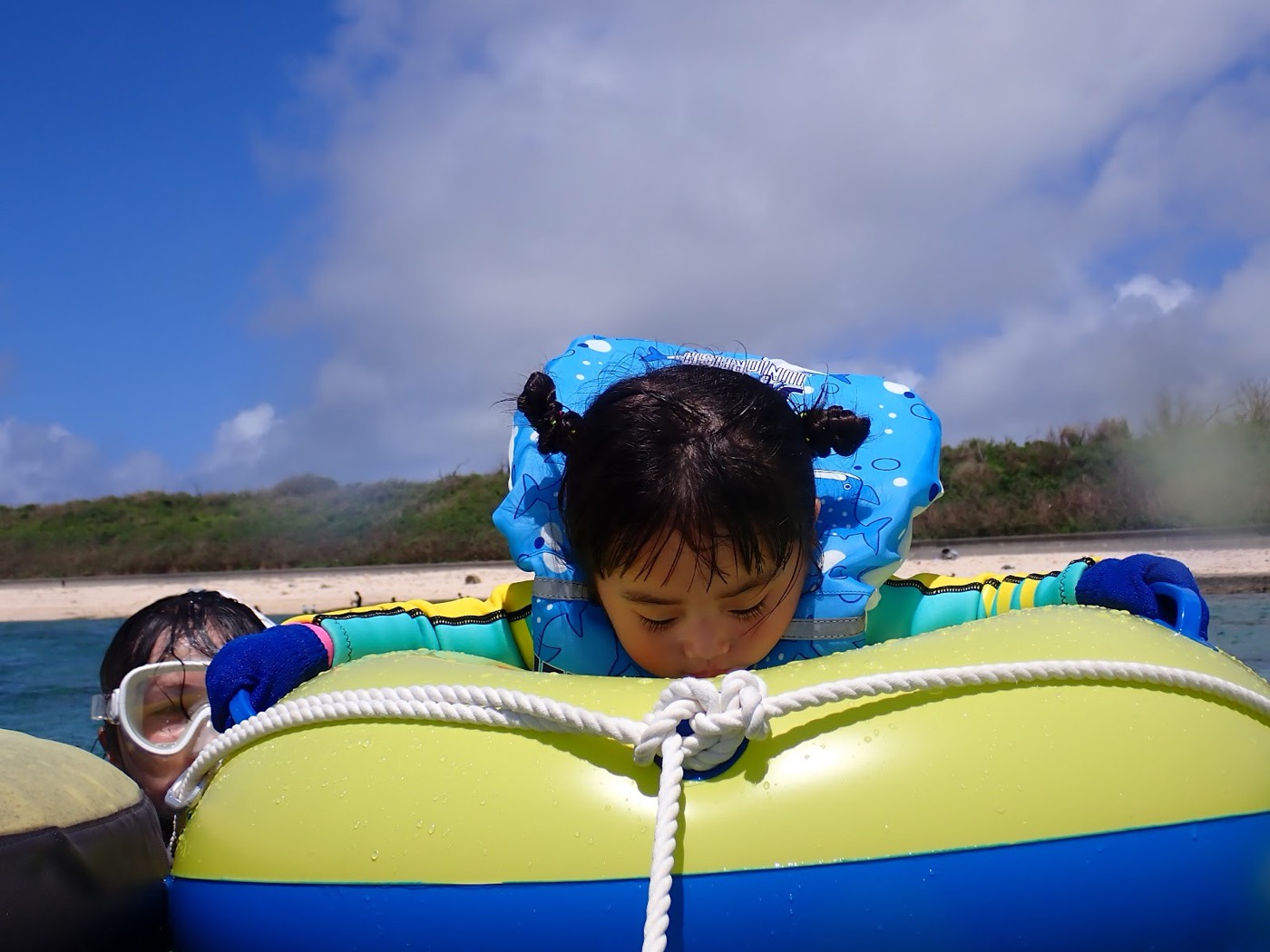 フロートにつかまり浅瀬で水面を覗き込む子供と、それを支えるガイド