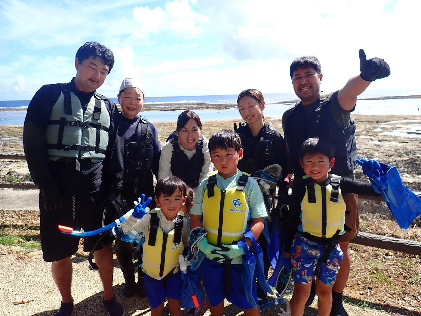 笑顔でポーズをとる参加者とガイド。背景には大度海岸が広がる