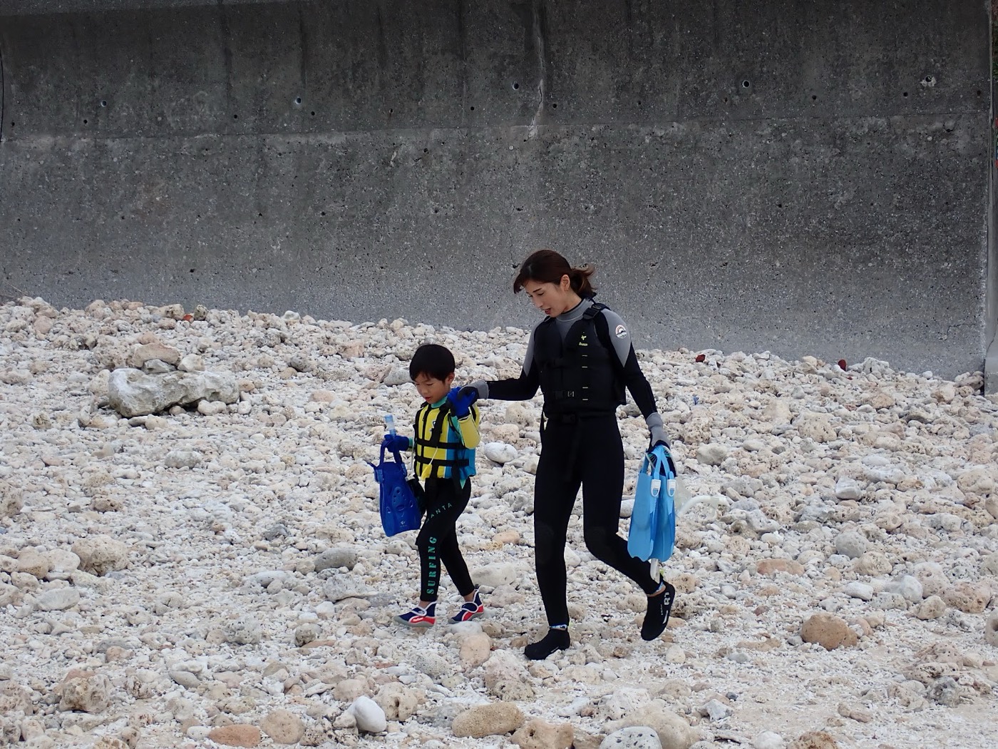 浜辺を歩く母親と小さなお子さん。担当の池田が少し離れた場所から見守っている